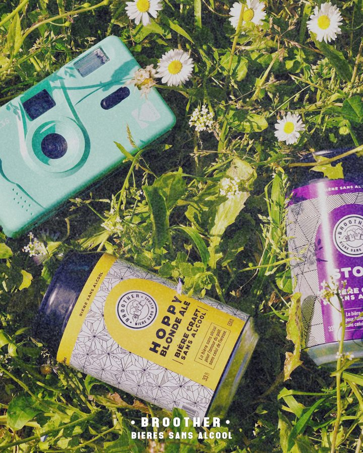 Canette BROOTHER Hoppy Blonde Ale allongée dans l'herbe parmi les pâquerettes avec un appareil photo jetable